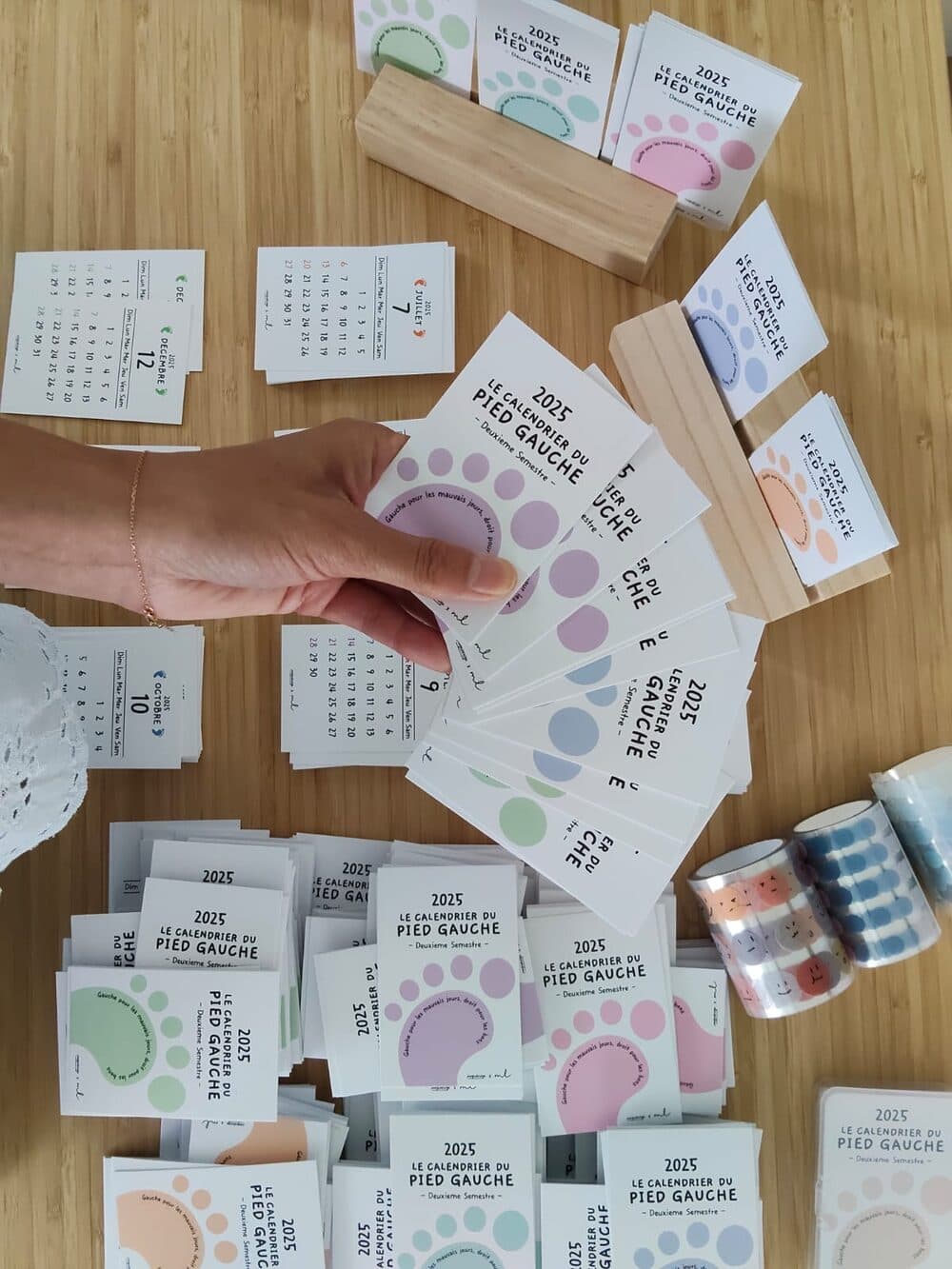 A hand fanning out cards of Le calendrier du pied gauche, in pastel colors